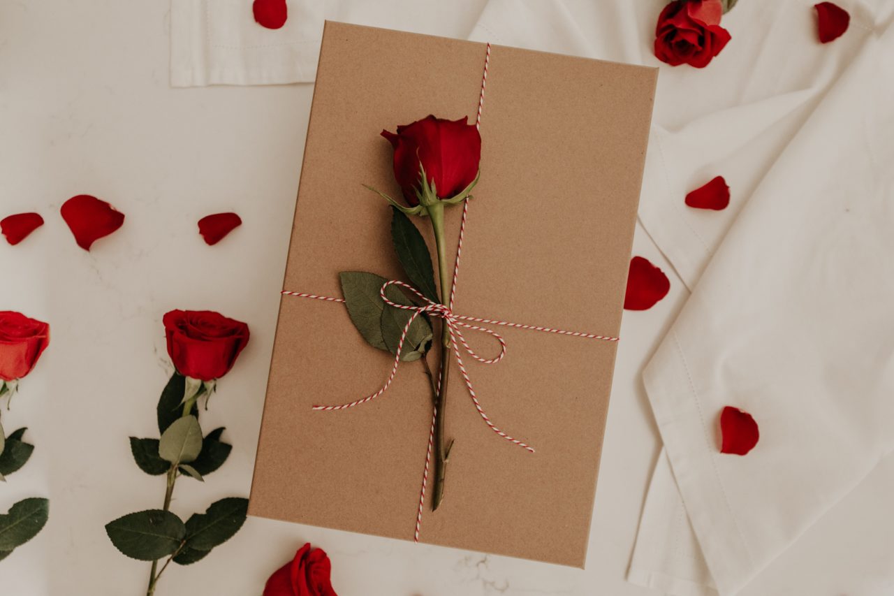 Idée-cadeau emballé avec une rose. Paquet posé sur un lit avec des pétales de fleurs pour le romantisme.